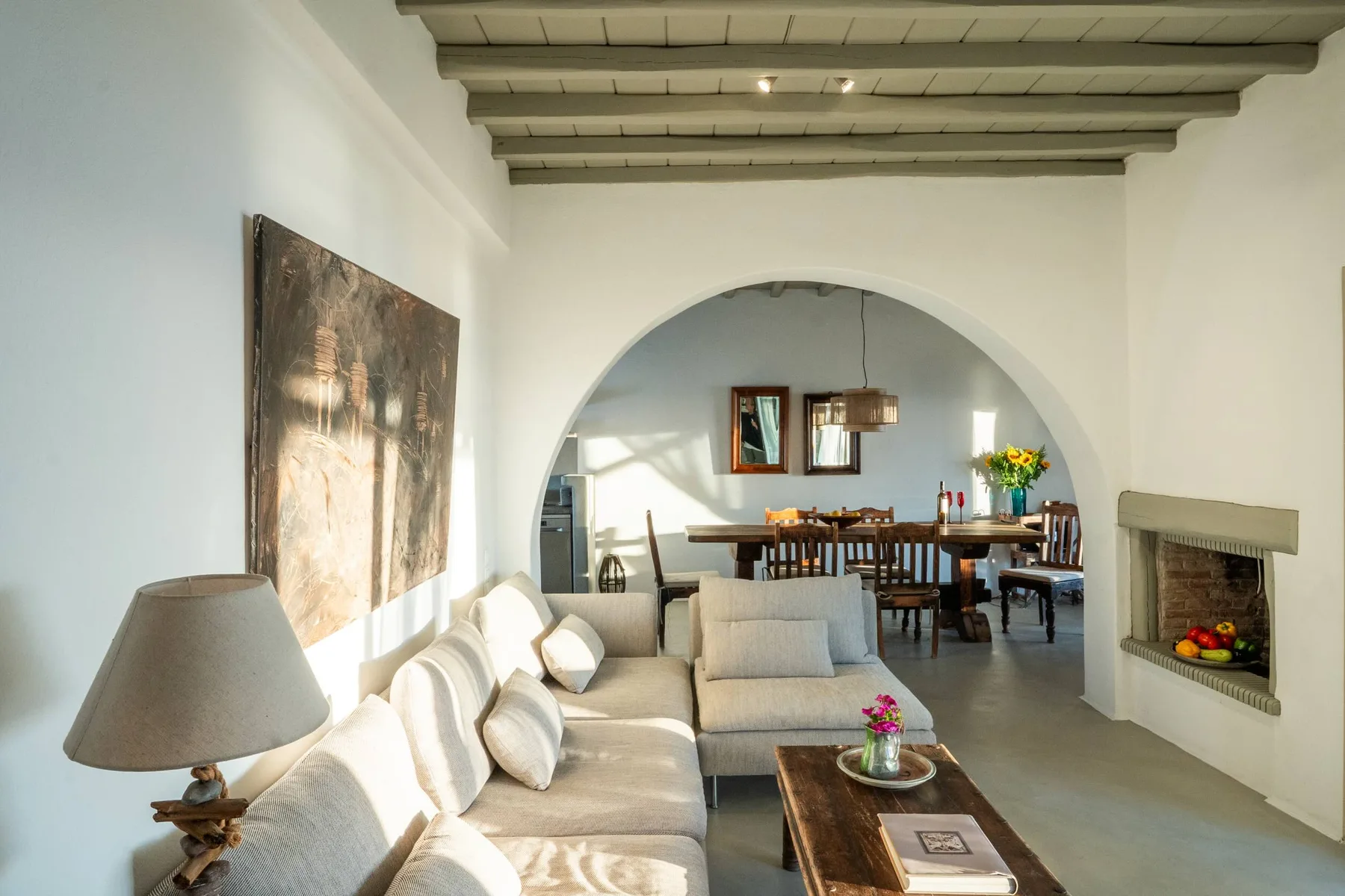 A living room with cushioned seating, a coffee table, and an arched opening to a dining area.