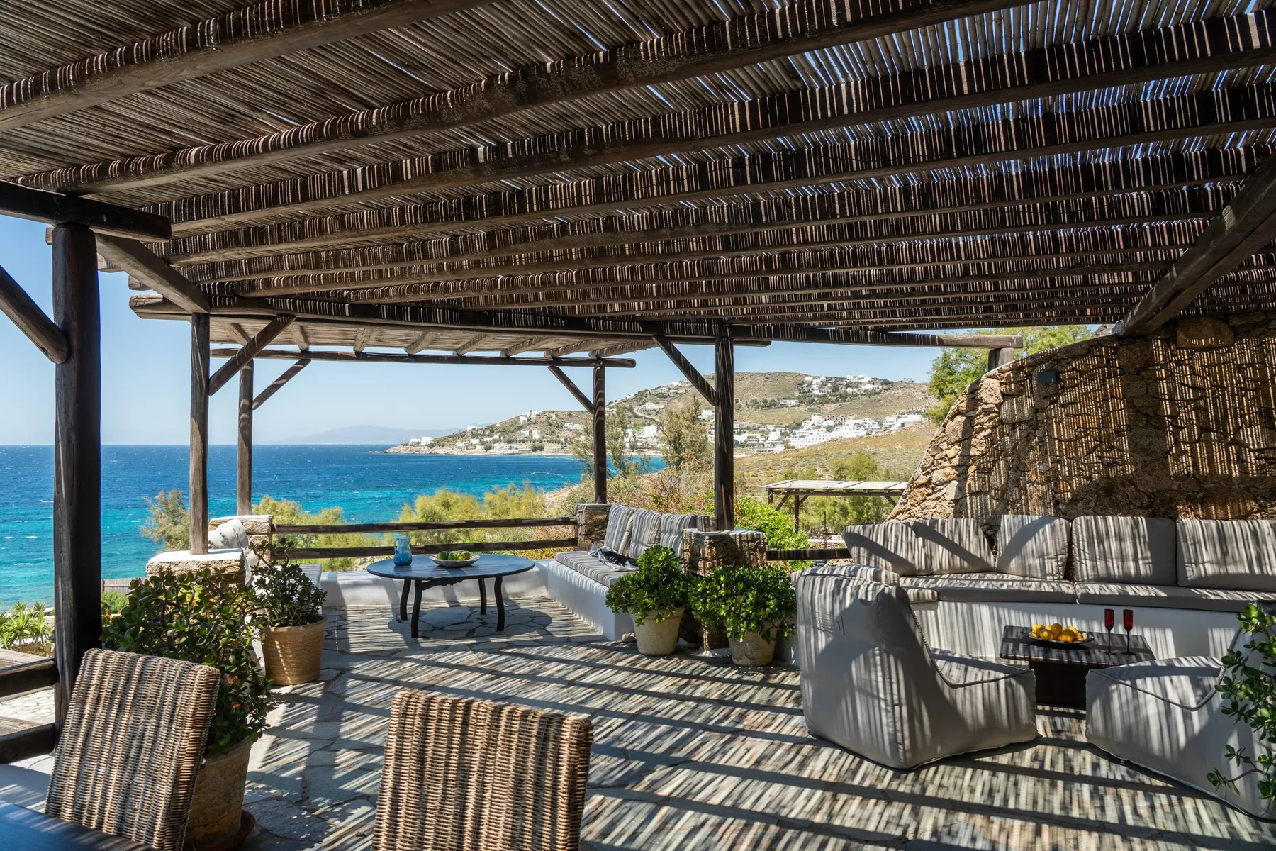 A shaded seaside terrace with outdoor seating and a view of the blue water.