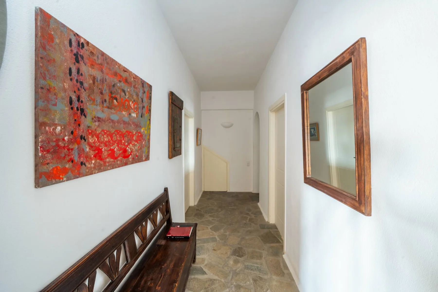 A narrow hallway with a wooden bench, framed artwork, and a mirror.