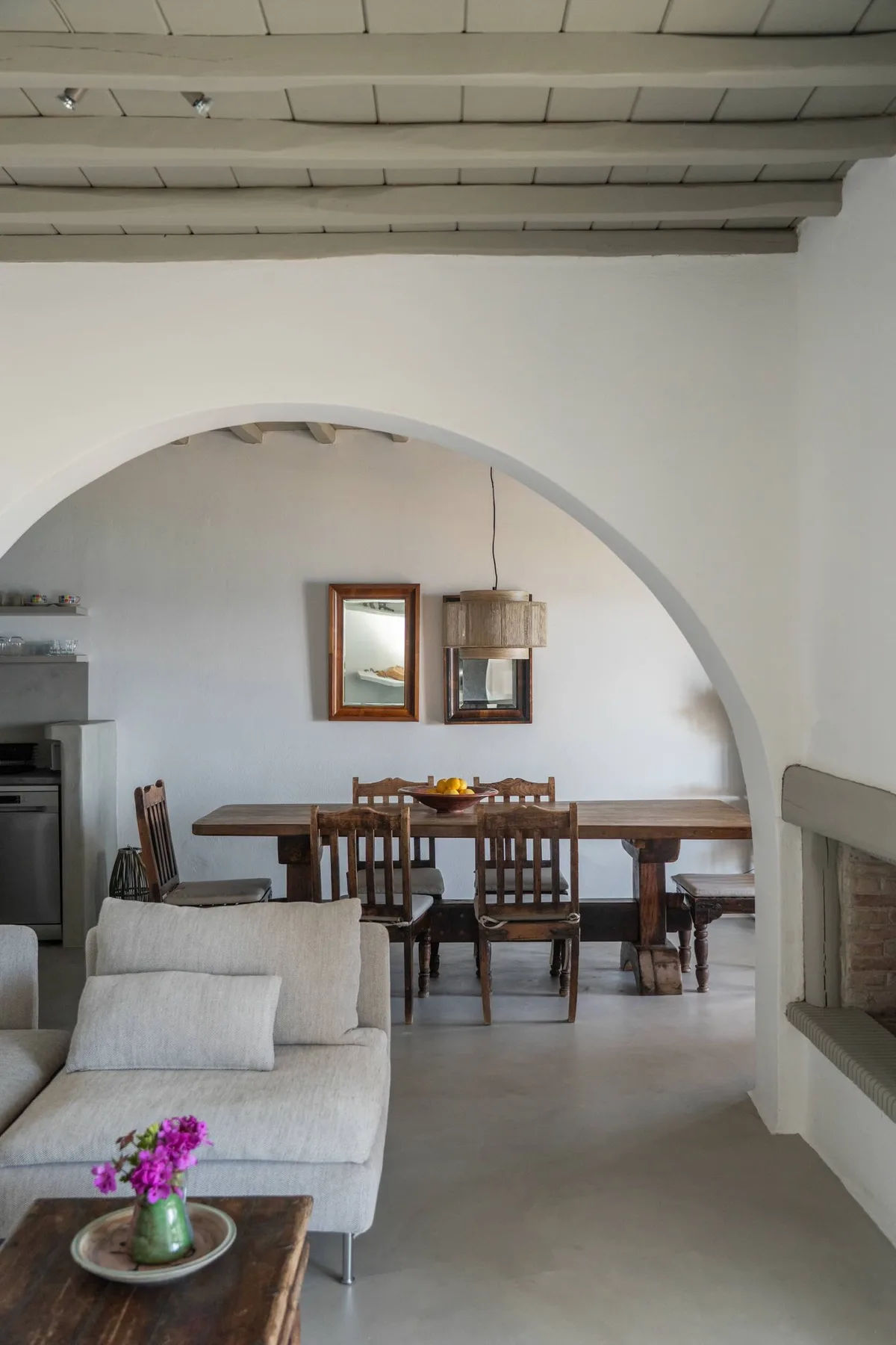 A dining area with a wooden table and chairs sits beyond an arched opening.