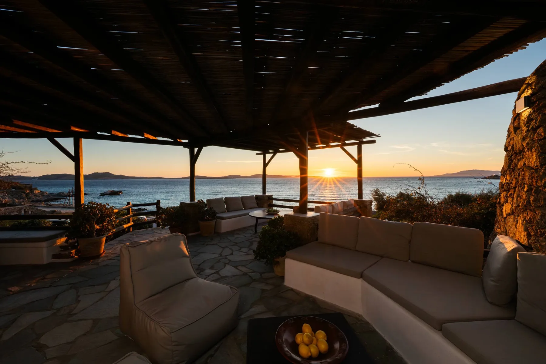 A covered outdoor seating area overlooks the water at sunset.