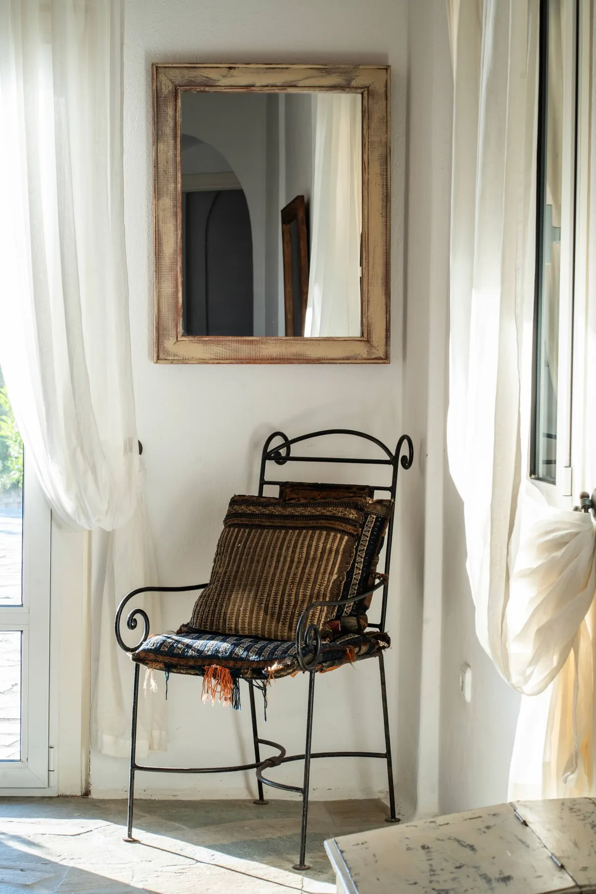 A metal-framed chair sits beneath a wall mirror in a bright room.