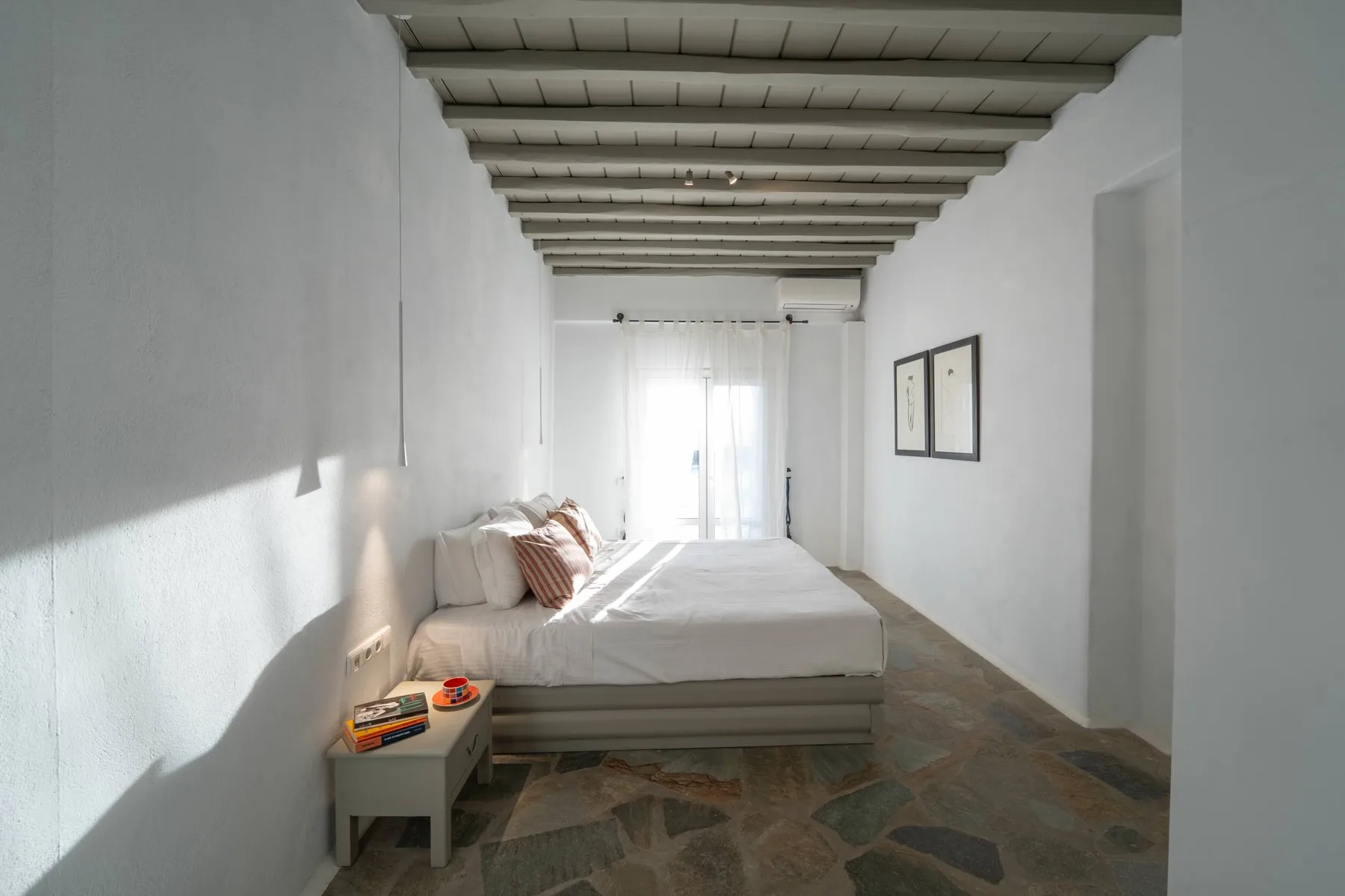 A bright bedroom with a bed, framed pictures, and exposed ceiling beams.