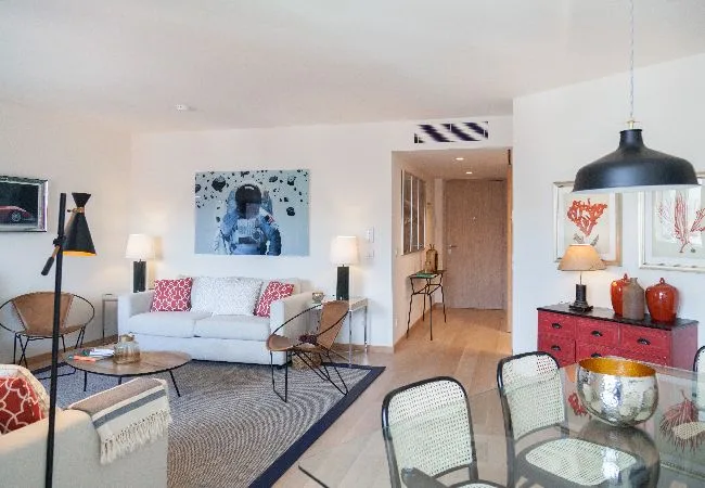 Una sala de estar con un sofá blanco, una alfombra y una mesa de comedor de vidrio.