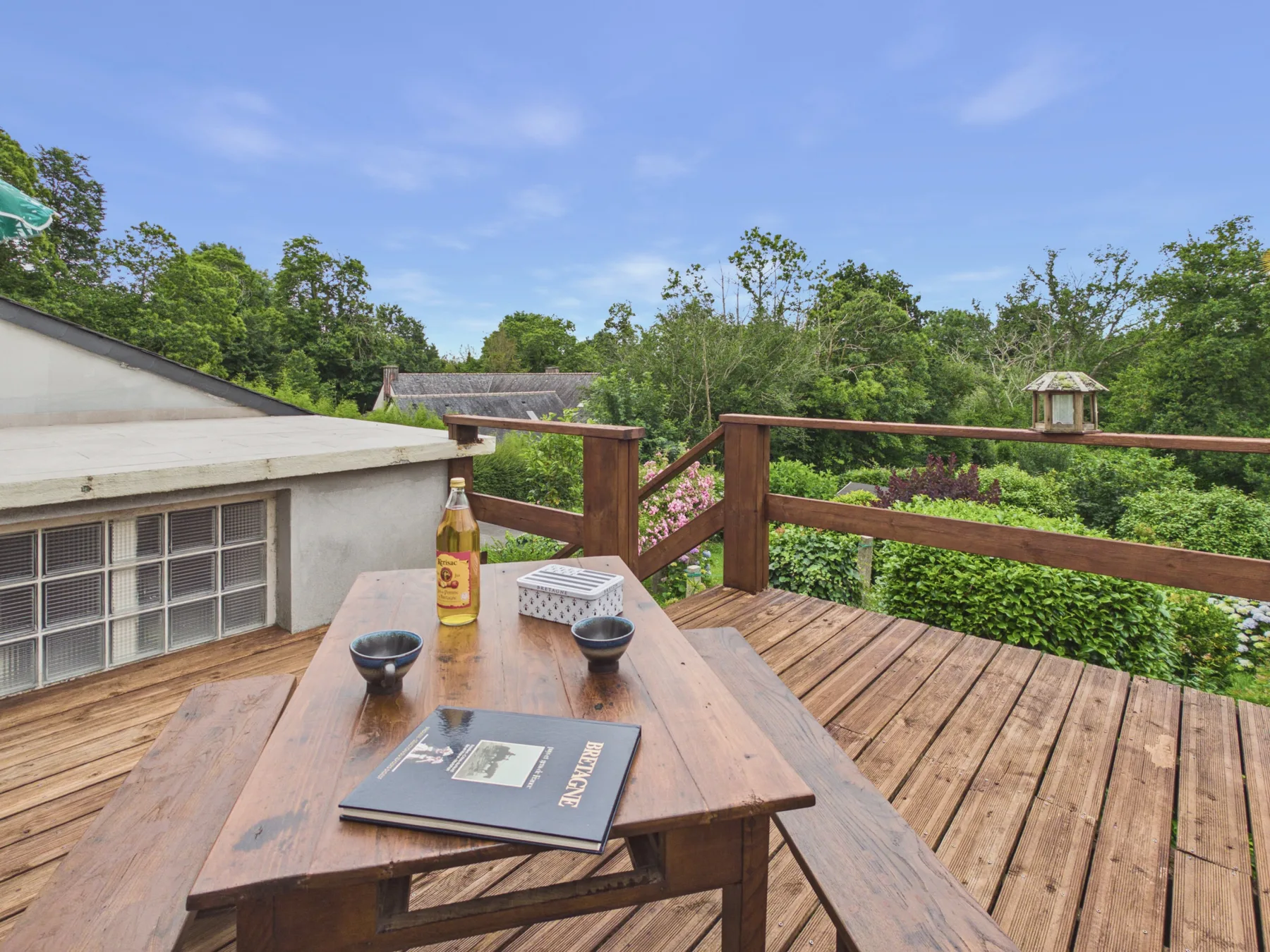 Una terraza de madera con una mesa da a un jardín frondoso.
