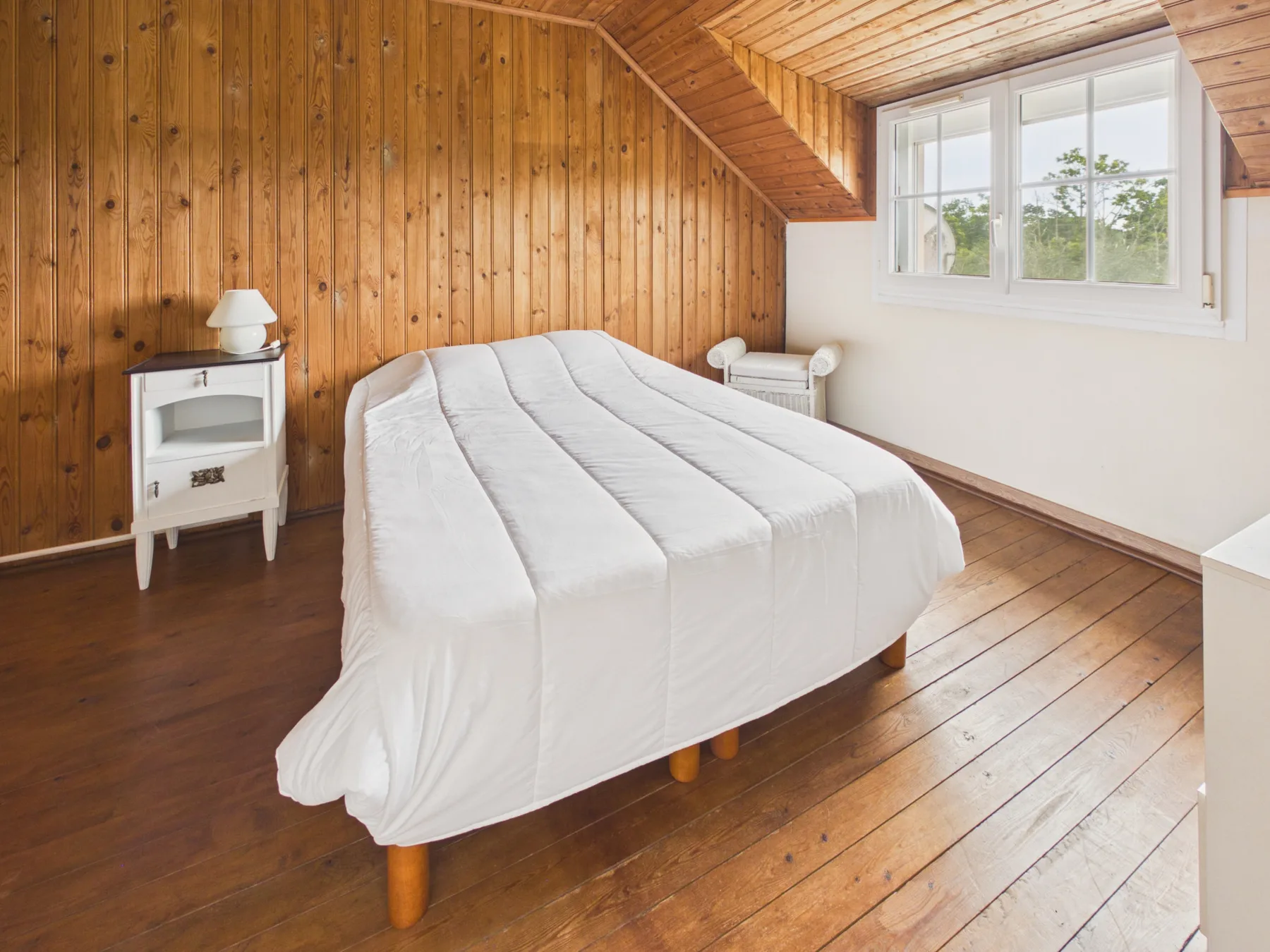 Un dormitorio con una cama bajo un techo inclinado de madera y una ventana.
