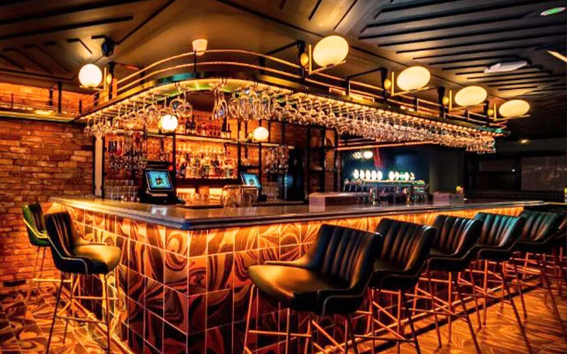 Espacio representativo del hotel: Un bar con iluminación cálida, una barra larga y filas de asientos.