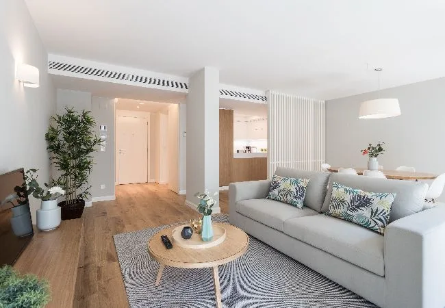 A bright living room with a light sofa, patterned rug, and round coffee table.