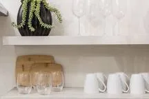 A light-colored shelf displays a potted plant and glassware.