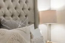 A bedroom seating area with a tufted upholstered headboard and bedside lamp.