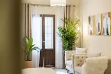 A living room with seating beside a tall window and indoor plants.