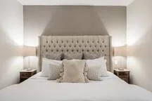 A bedroom with a tufted headboard, white bedding, and matching bedside tables.