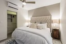 A bedroom with a neatly made bed and a padded headboard.