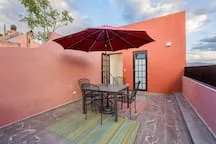A rooftop patio has a dining table and chairs beneath a red umbrella.
