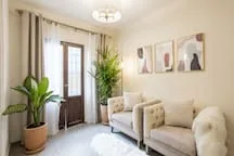 A bright living room with cream seating, plants, and framed wall art.