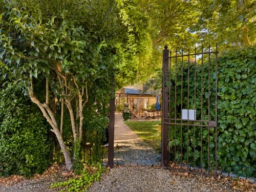 Espacio representativo del hotel: Un sendero de jardín atraviesa una puerta metálica abierta y conduce a una zona de asientos al aire libre.