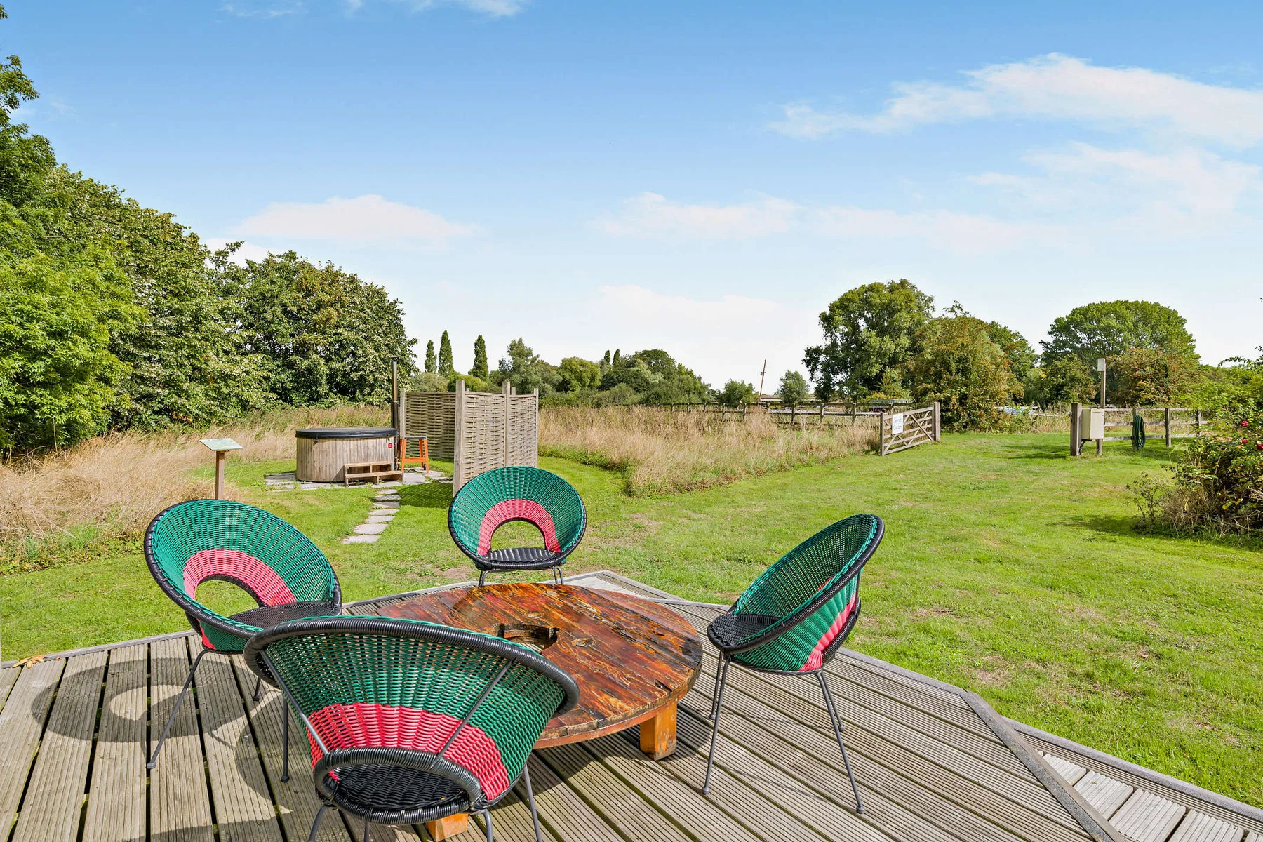 An outdoor deck with colorful woven seating overlooks a grassy yard.