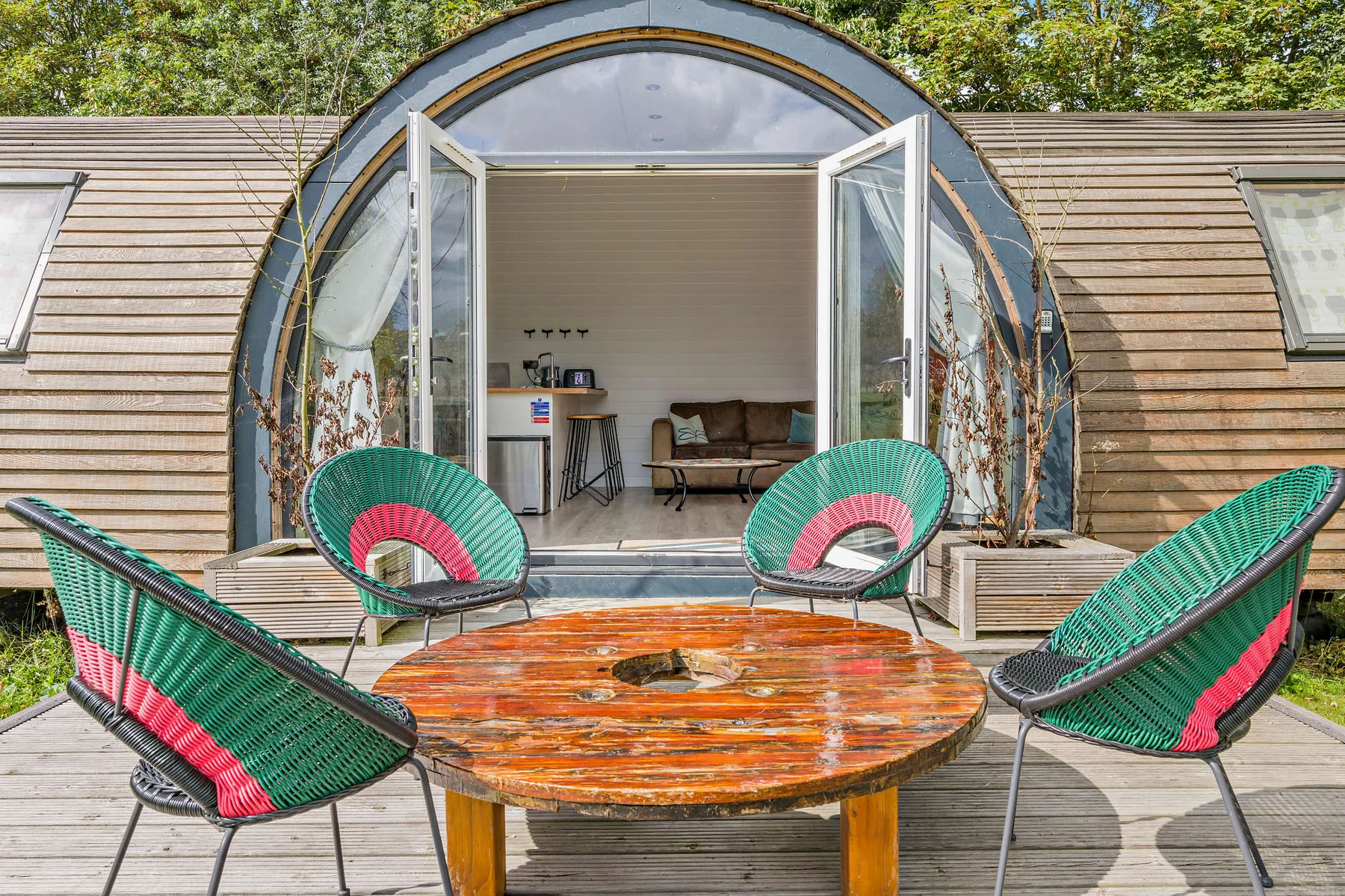 An arched cabin entrance opens onto a wooden deck with colorful woven seating.