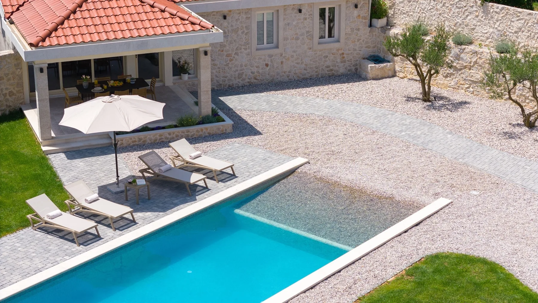 Una piscina en un patio está junto a una terraza cubierta y un edificio de piedra.