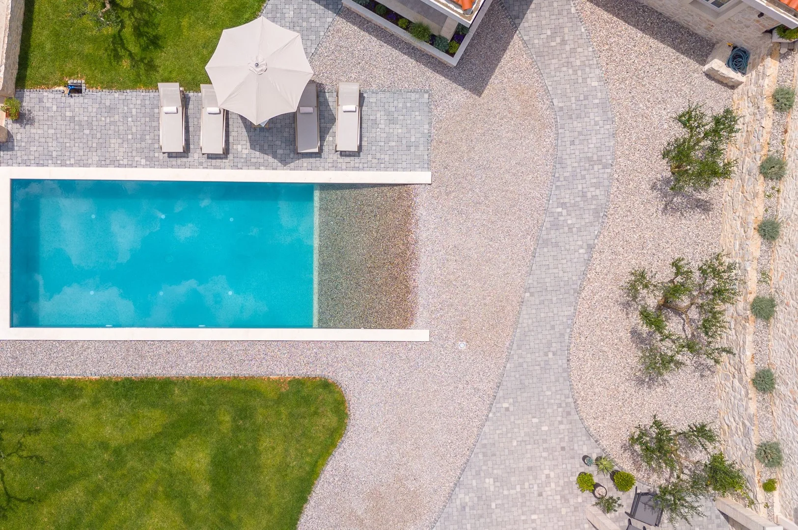 Vista aérea de una piscina al aire libre junto a caminos pavimentados y jardines.