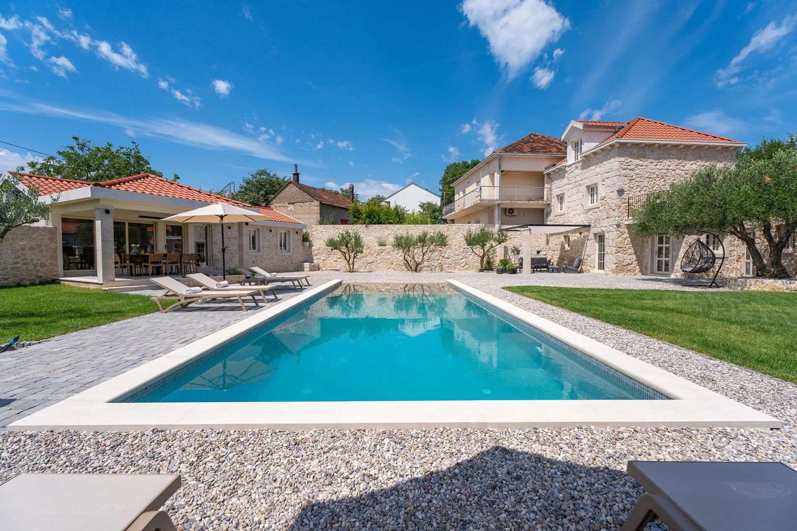 Una piscina al aire libre junto a una casa de piedra y un patio cubierto.