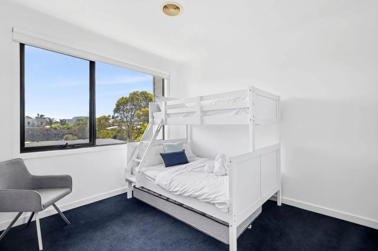 A bright bedroom has a white bunk bed beside a large window.