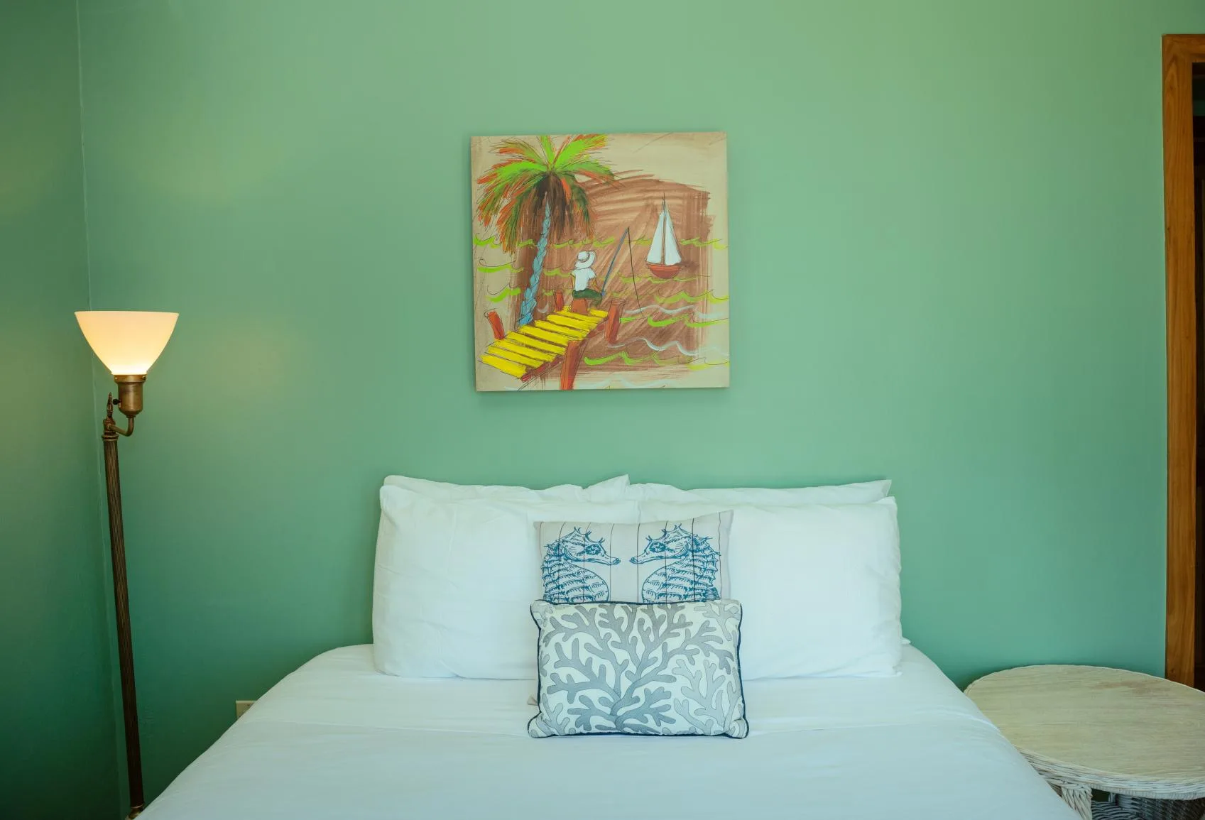 A bedroom with a bed, a patterned accent pillow, and tropical wall art.