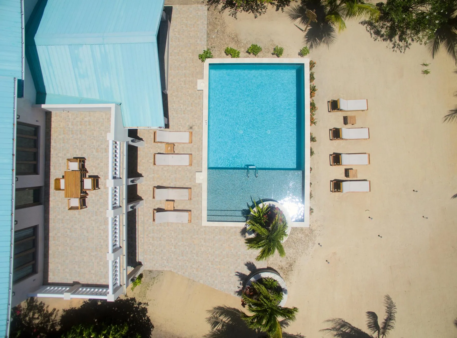 An aerial view shows a rectangular swimming pool beside a sandy beach.