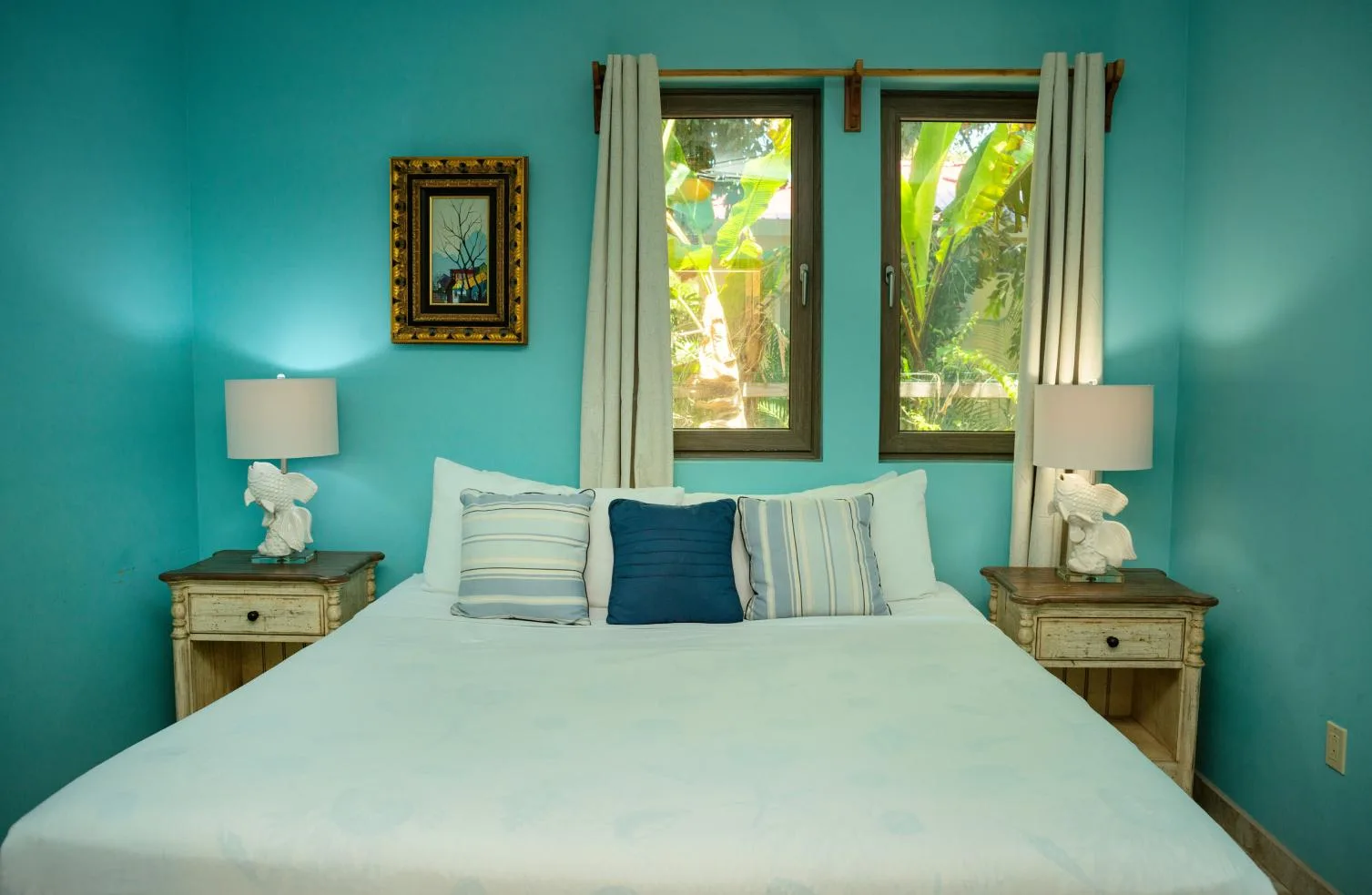 A bedroom with a bed between two nightstands and a window overlooking greenery.