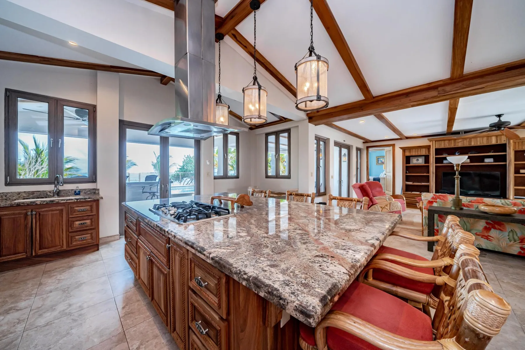 A spacious kitchen and living area with a large stone island and exposed ceiling beams.