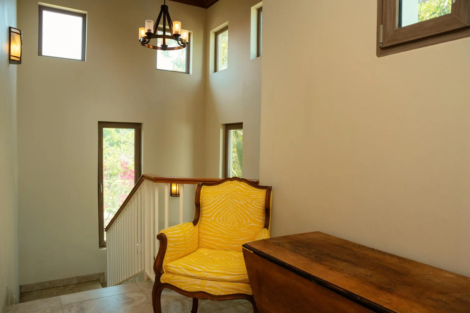 A bright sitting area has a yellow upholstered chair beside a wooden table.
