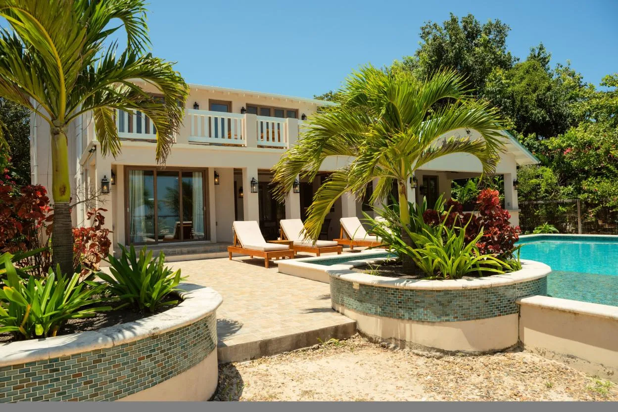 A sunny poolside patio with lounge seating and tropical plants.