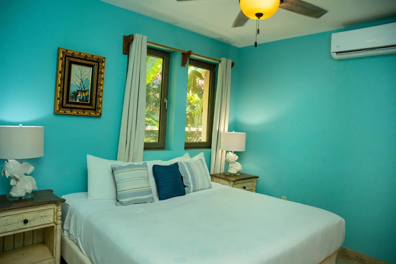 A bedroom with a bed, turquoise walls, and windows overlooking greenery.