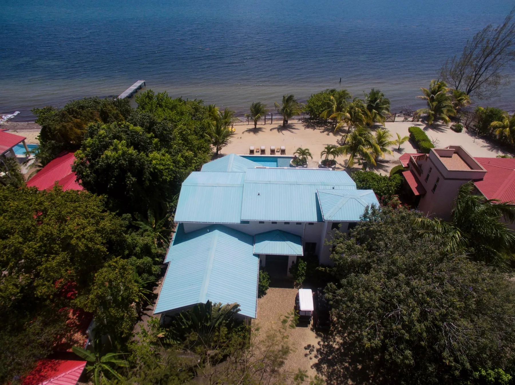 An aerial view of a light-colored building among trees beside a beach and calm water.