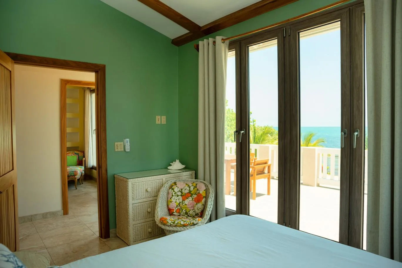 A bedroom with green walls, a bed, and glass doors opening onto a balcony.