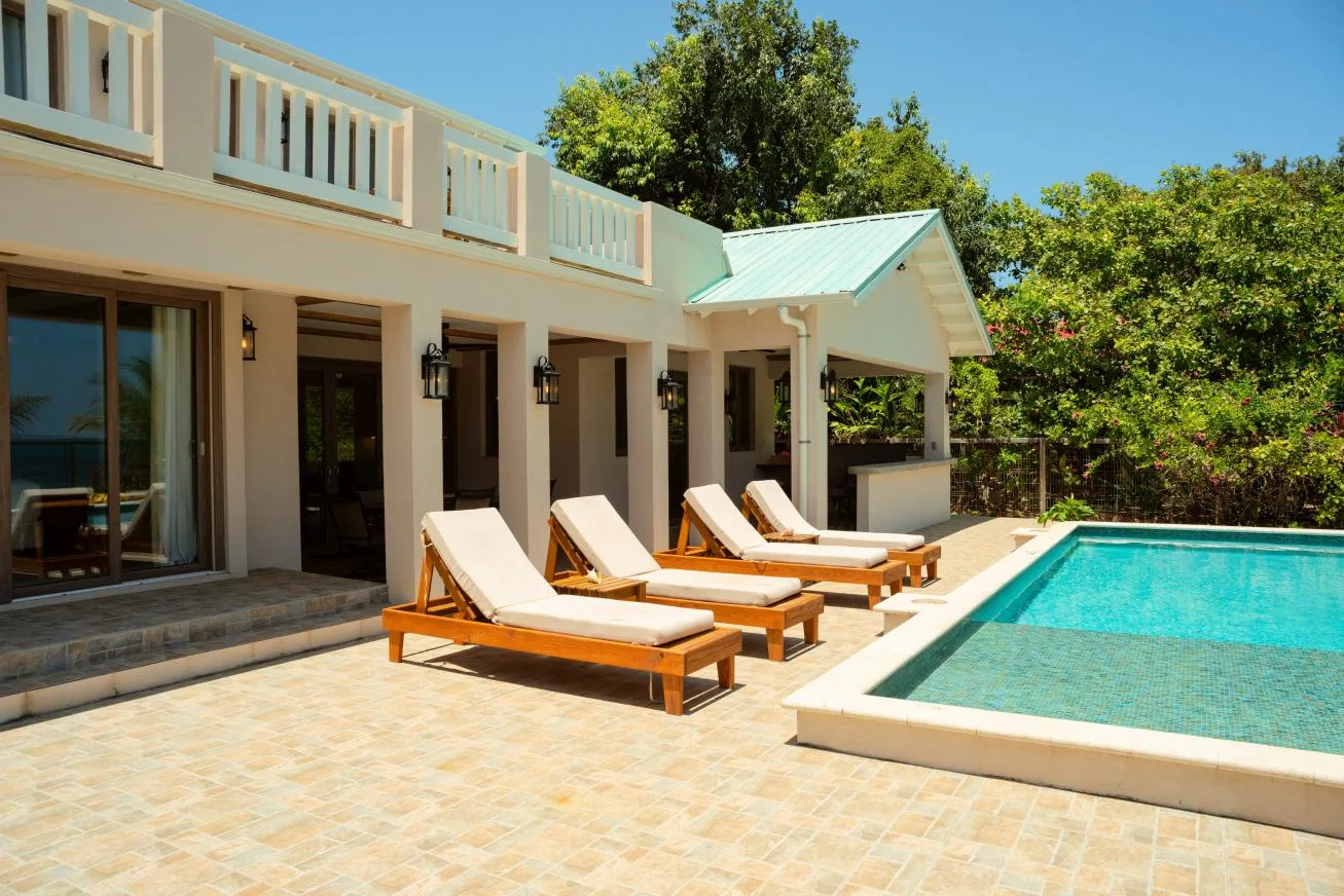 A patio beside a swimming pool, with lounge seating outside a light-colored building.