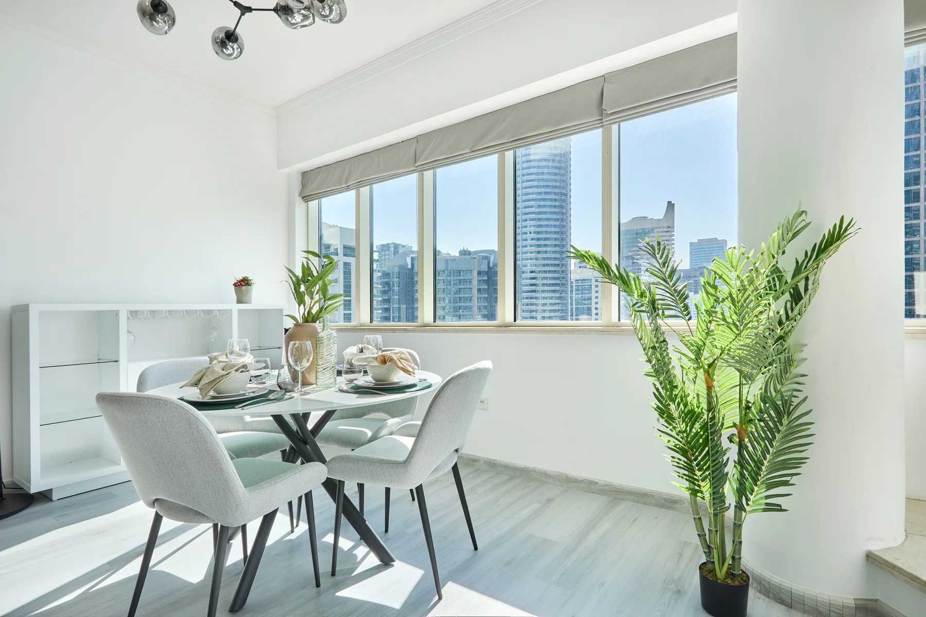 Un comedor luminoso con la mesa puesta junto a grandes ventanales con vistas a la ciudad.