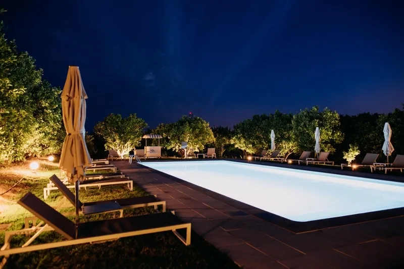 Representative hotel space: An outdoor swimming pool at night, bordered by lounge seating and greenery.