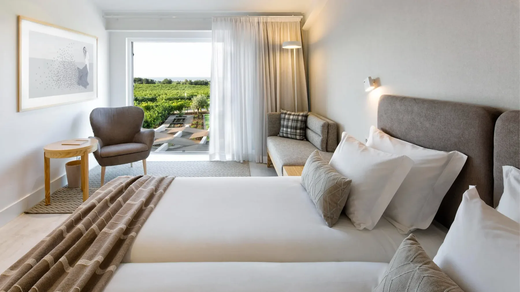 Representative hotel space: A bright bedroom with a neatly made bed and seating beside a large window.