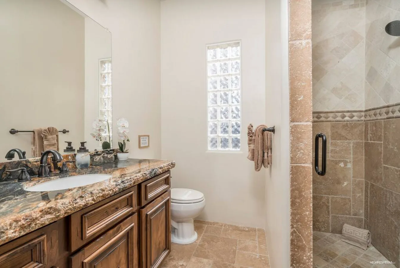 A bathroom with a long vanity, a toilet, and a glass-block window.