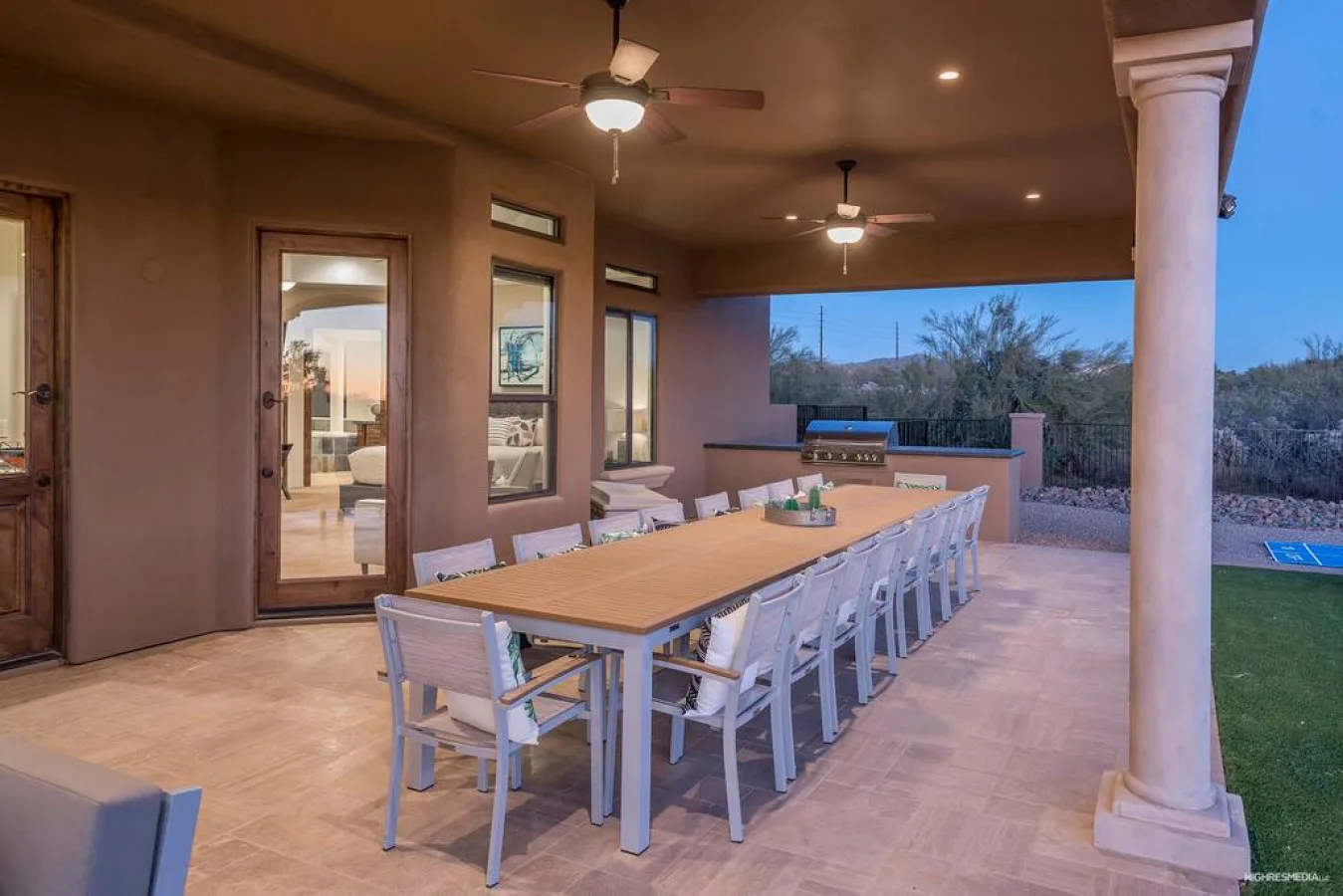 A covered patio dining area with a long table and views of the garden.