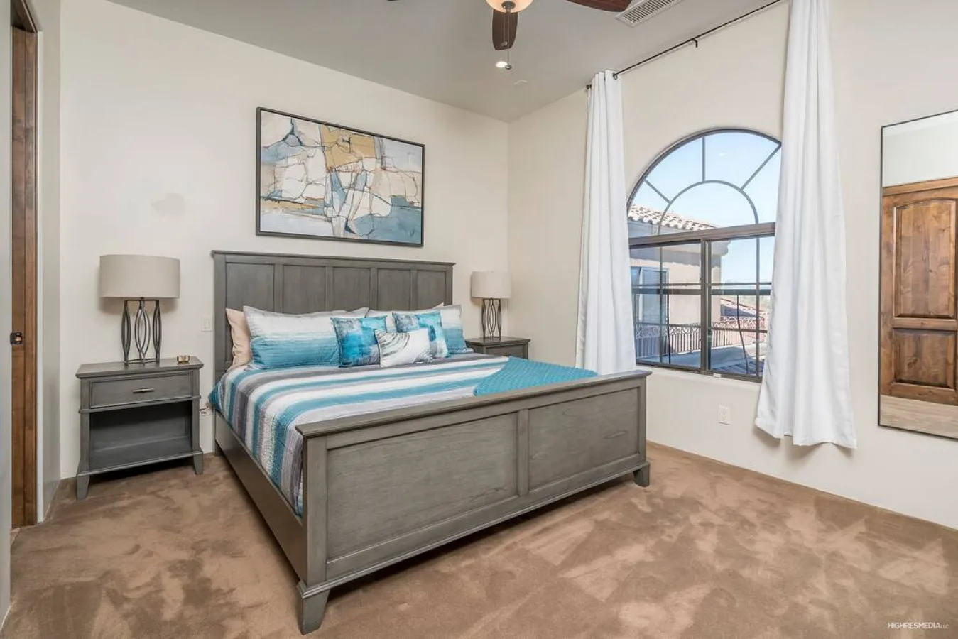 A bedroom with a bed dressed in blue and white bedding beside a large arched window.