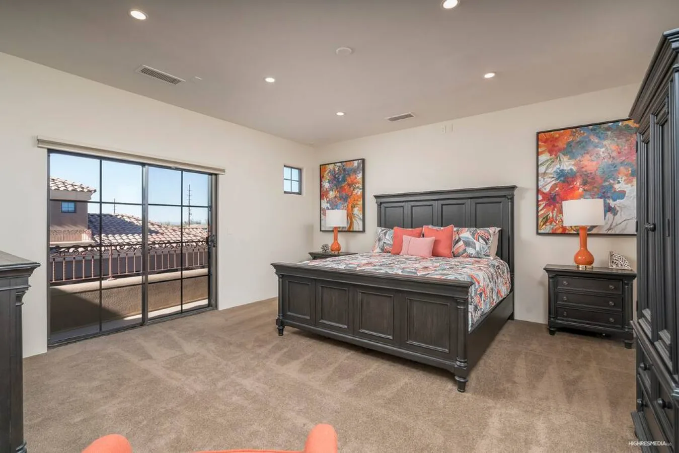 A bedroom with a large bed, colorful artwork, and glass doors opening to a balcony.