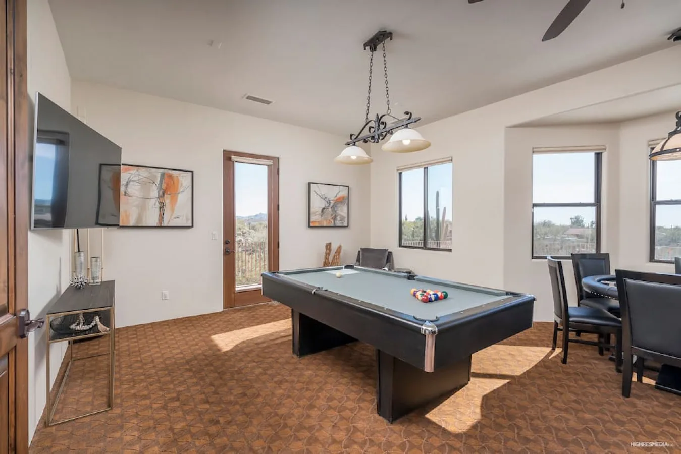 A game room with a pool table and seating by the windows.