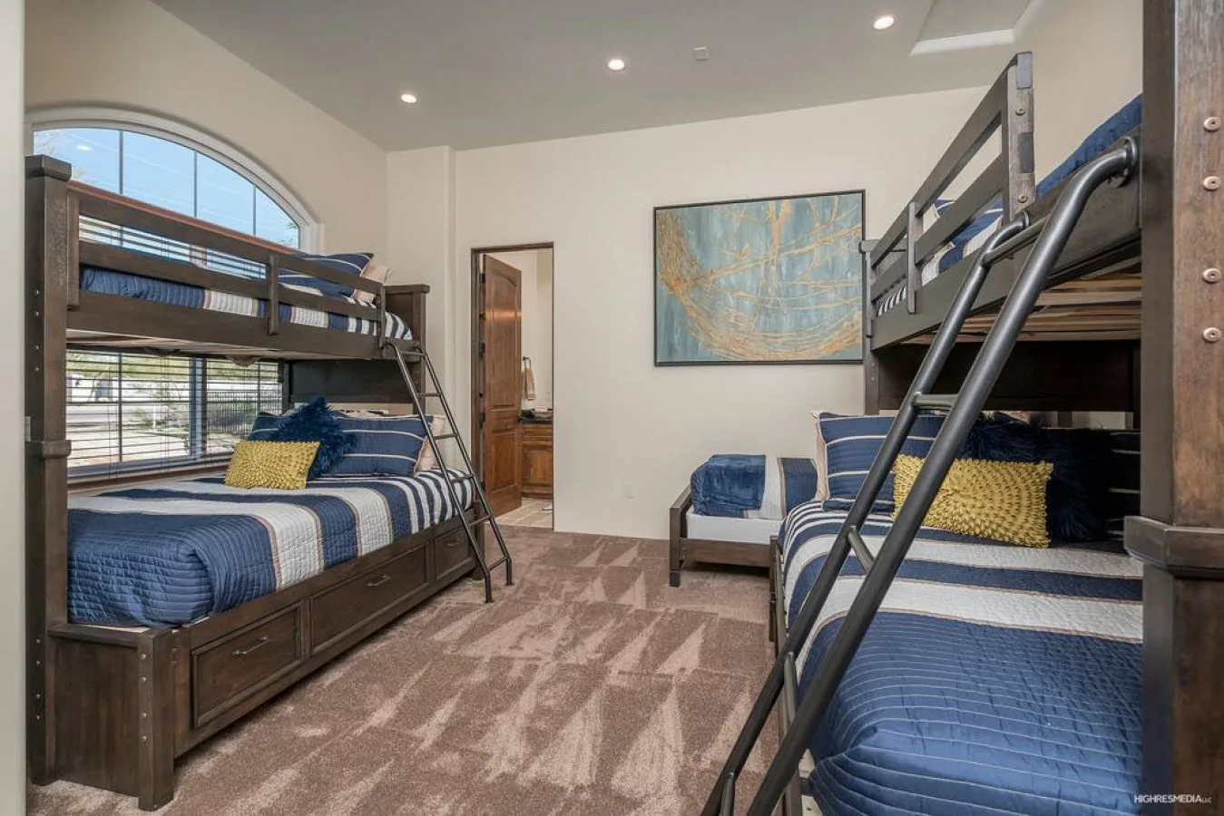 A bedroom with bunk beds and blue bedding, with a large arched window.