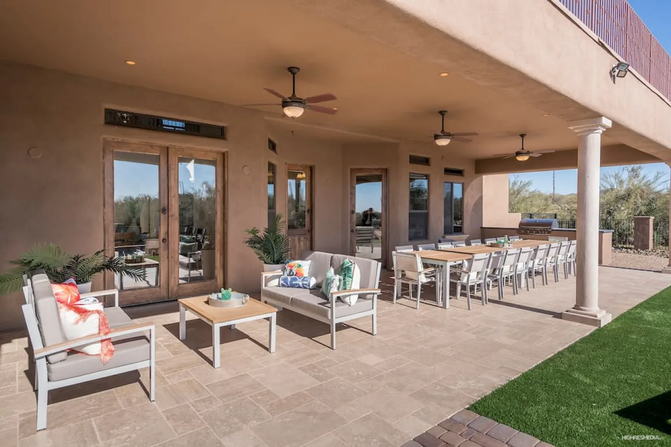 A covered patio has lounge seating and a long outdoor dining table.