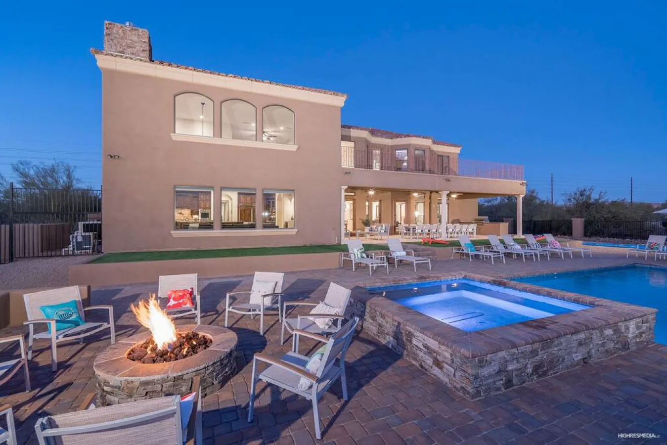 An outdoor pool and patio with seating, a fire pit, and a large building in the background.
