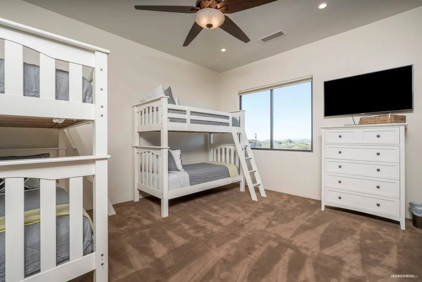A bedroom with bunk beds, a window, and a dresser topped by a television.