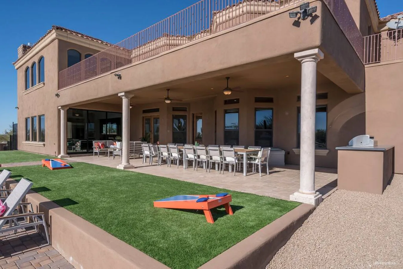 A covered patio with outdoor dining tables overlooks a small artificial-turf lawn.
