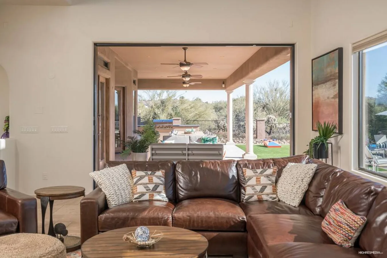 A living room with brown seating faces an open patio and garden.